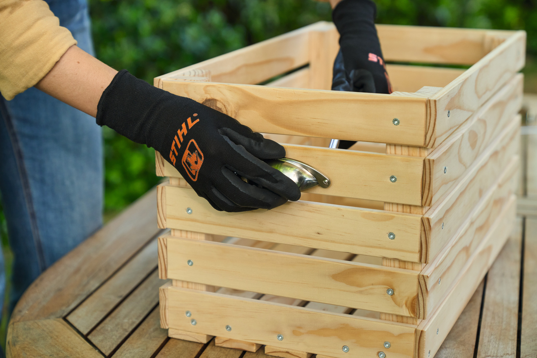 Eine Person schraubt seitliche Handgriffe an den Schmalseiten des Blumenkastens an