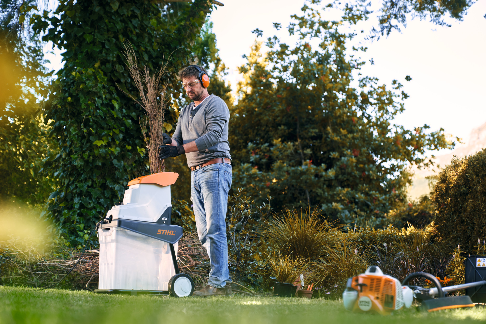 Mann mit STIHL Benzin-Häcksler zwischen Bäumen und Sträuchern vor einem Haus