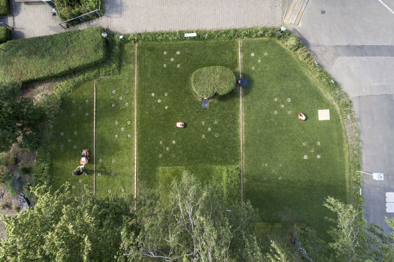 Blick von oben auf ein in vier Teile unterteiltes Grundstück mit STIHL Mährobotern und einem Rasenmäher auf dem Werksgelände