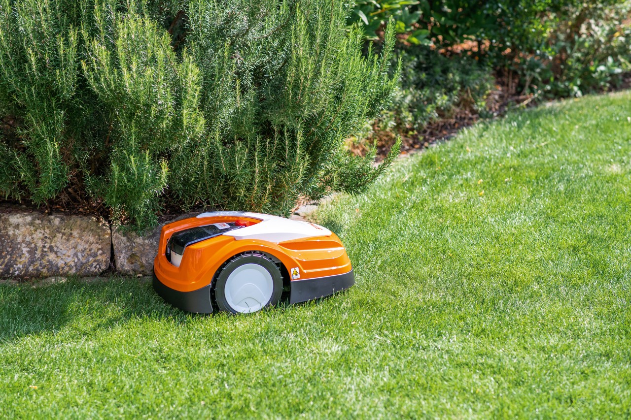 STIHL Mähroboter iMOW® RMI 422 PC auf grünem Rasen neben einer Beetbegrenzung aus flachen Steinen