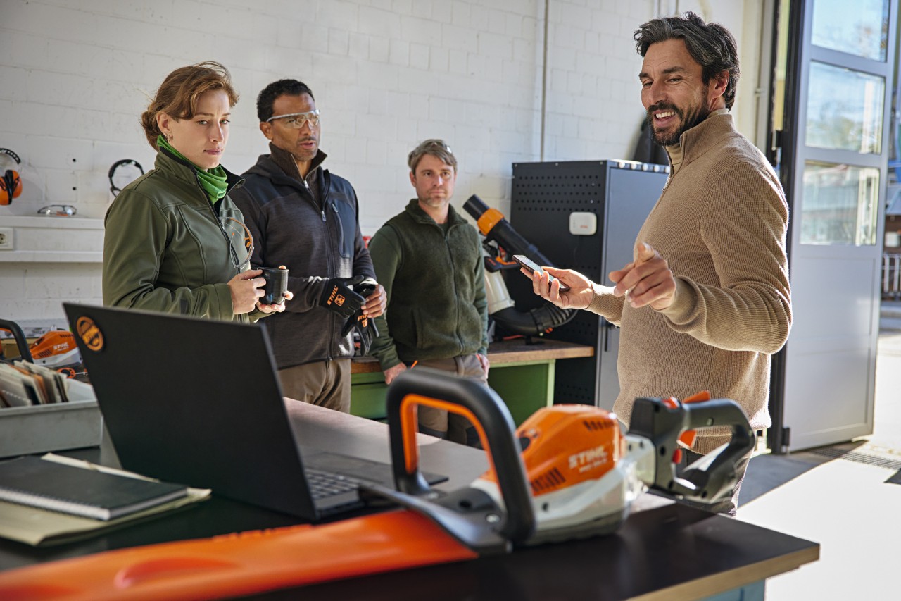 Ein Team von Landschaftsgärtnern bespricht seine Arbeit in einer Lagerhalle mit Hilfe der STIHL connected App auf dem Smartphone