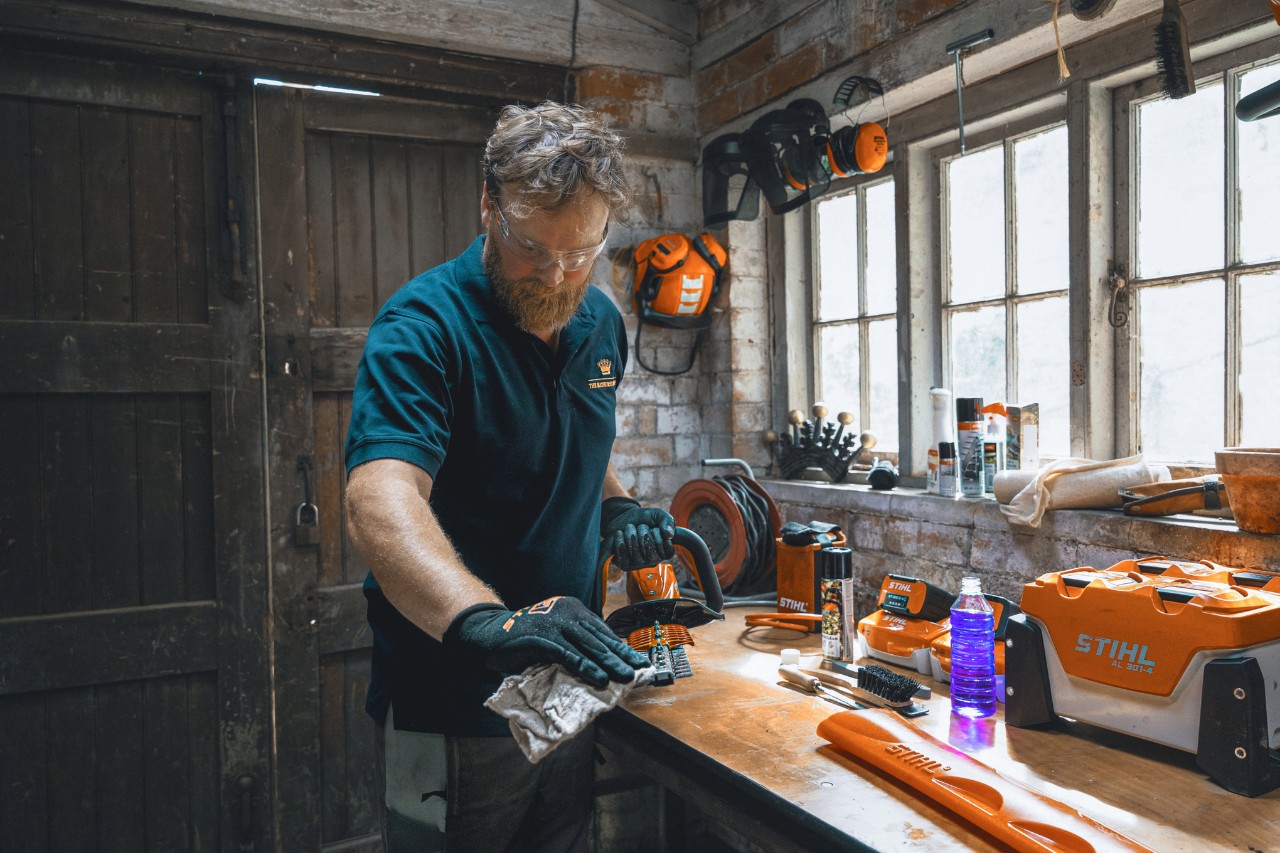 Ein Mann in einer Werkstatt wischt mit einem Tuch eine STIHL Heckenschere ab