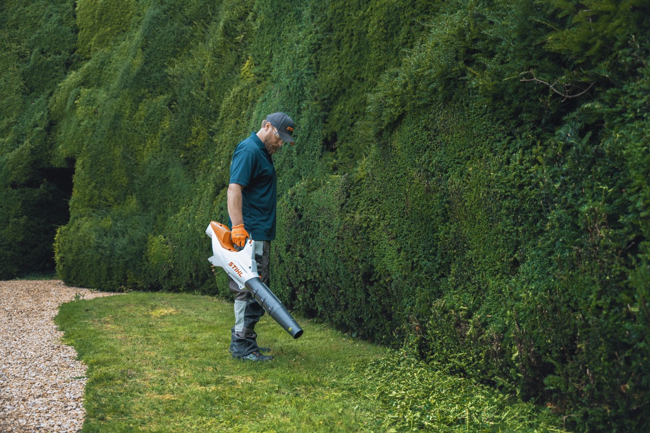 Ein Profi steht mit einem STIHL Akku-Laubbläser vor der hohen Hecke von Bathurst Estate
