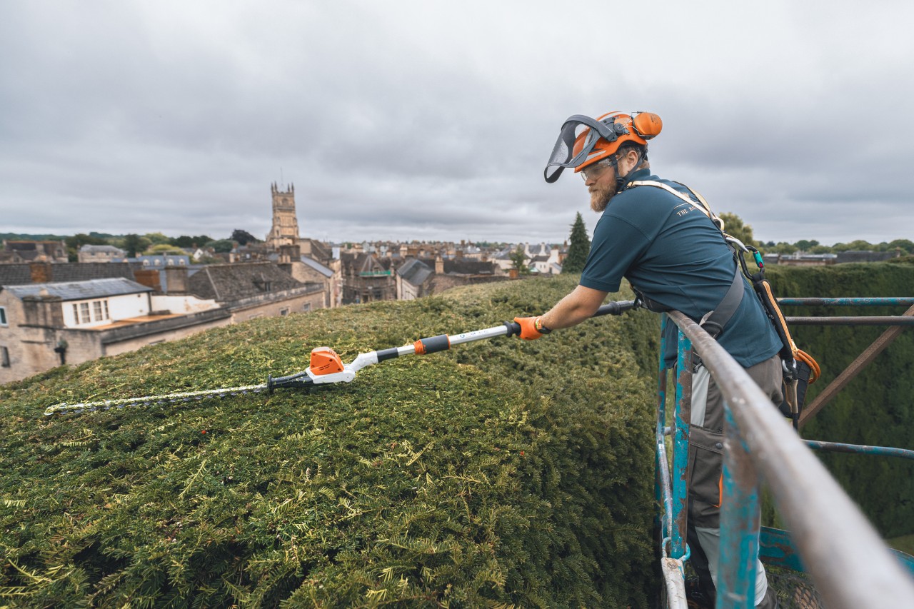 Ein Profi schneidet mit einem STIHL Akku-Heckenschneider auf einer Hebebühne die Oberseite der Hecke des Bathurst Estate