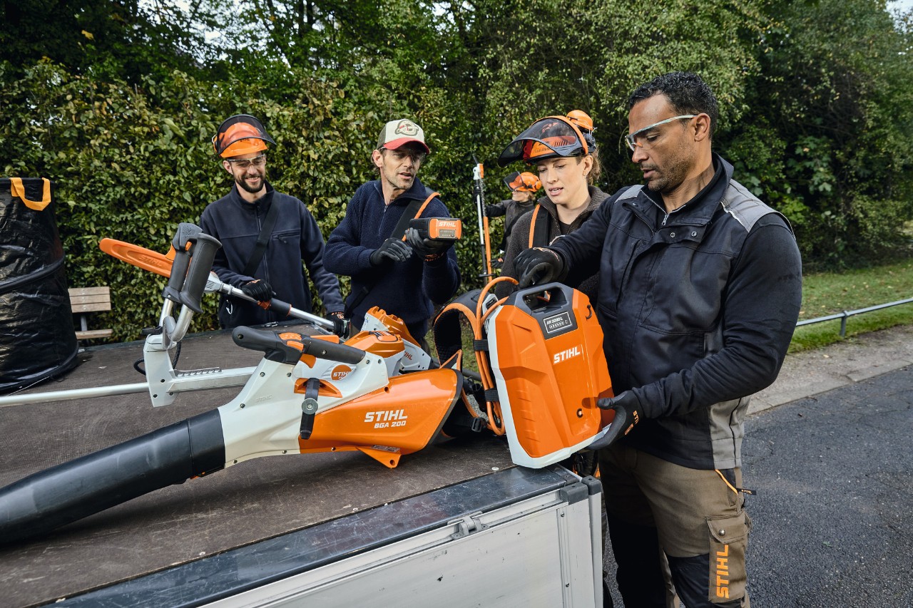 Drei Männer und eine Frau in STIHL Schutzausrüstung stehen an der Ladefläche eines Fahrzeugs mit STIHL Geräten, wie zum Beispiel der Akku-Laubbläser STIHL BGA 200 und der rückentragbare Akku STIHL AR 2000 L 