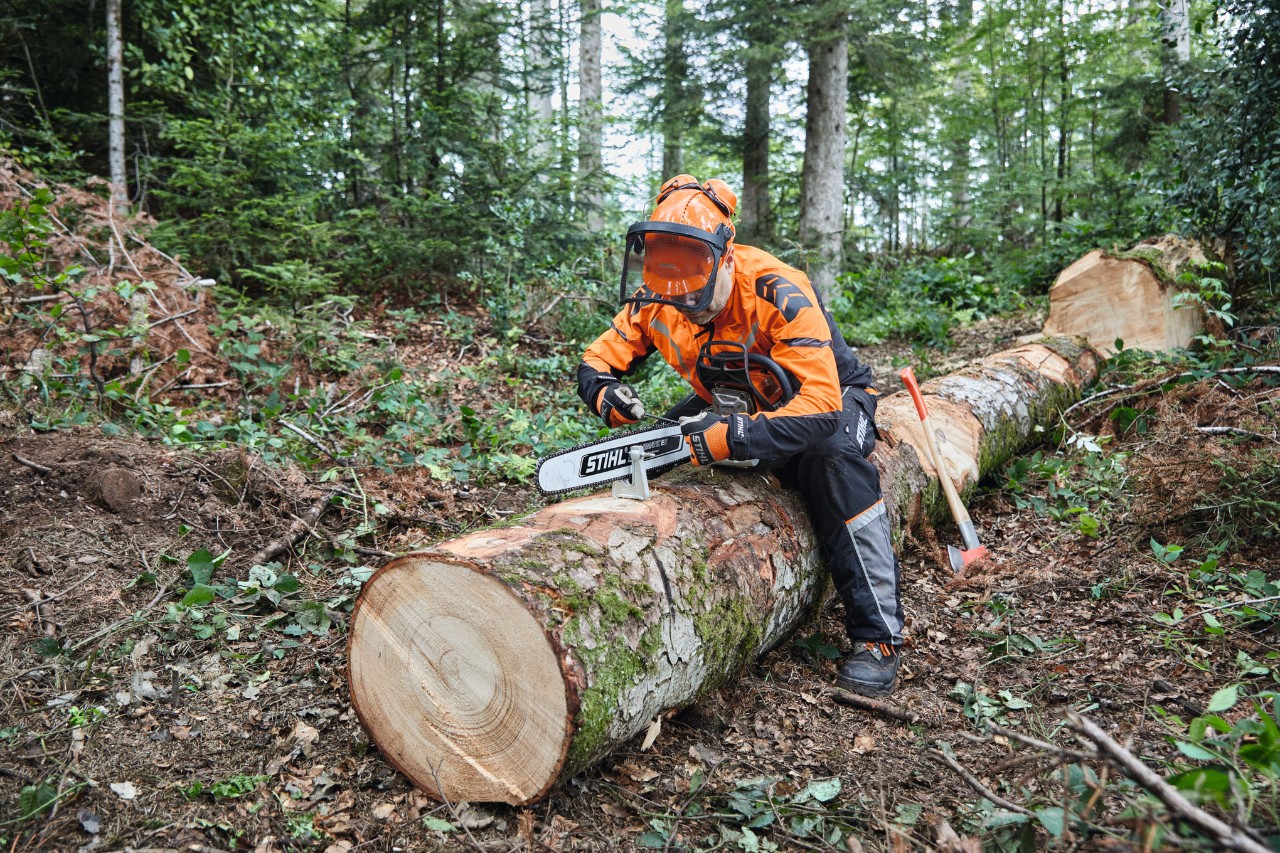 Ein Mann in Schutzausrüstung zerlegt mit einer STIHL Kettensäge mit Vollschiene einen bereits gefällten Baum