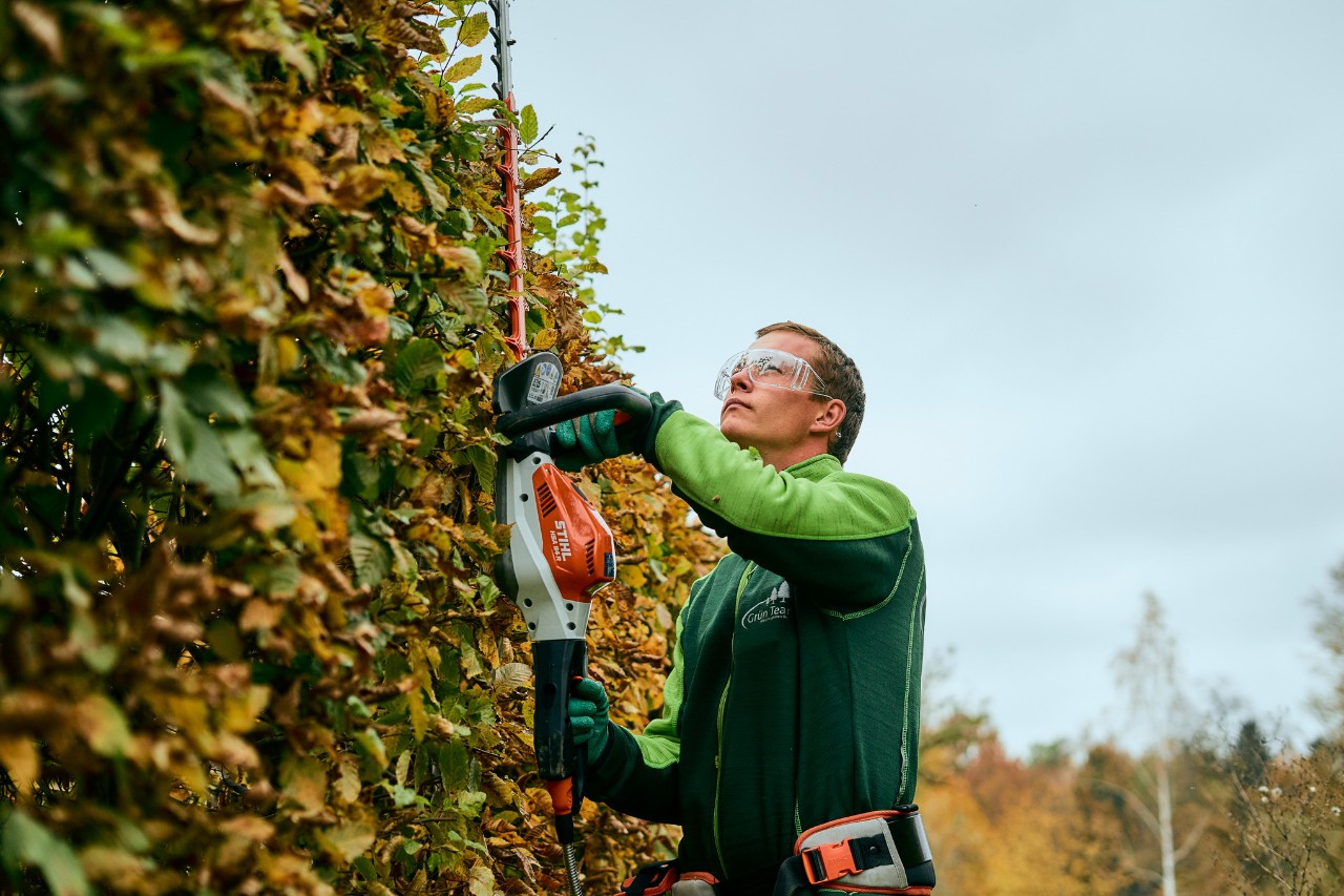 Mann schneidet Hecke mit STIHL Gerät mit angeschlossenem