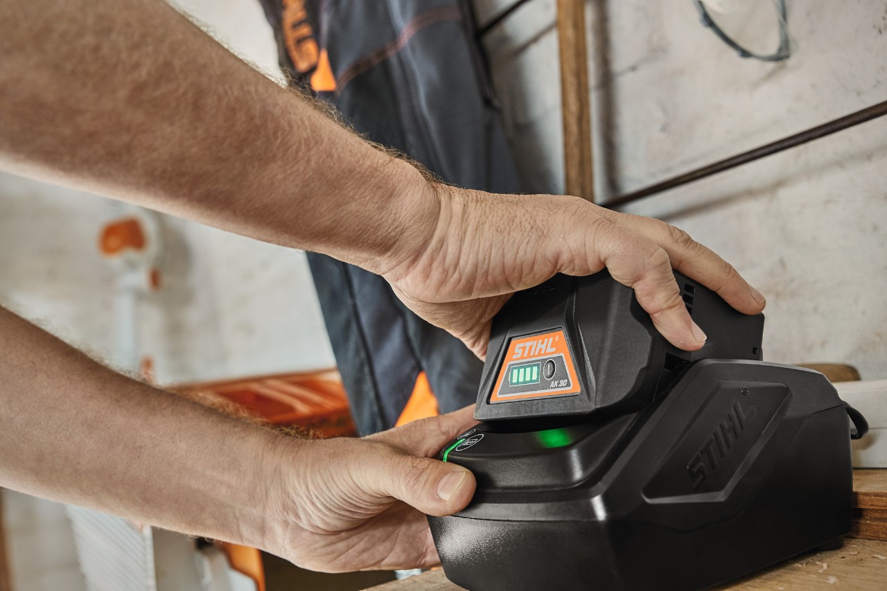 Ein Mann schließt einen Akku STIHL AK 30 an ein Standard-Ladegerät STIHL AL 101 an, Nahaufnahme