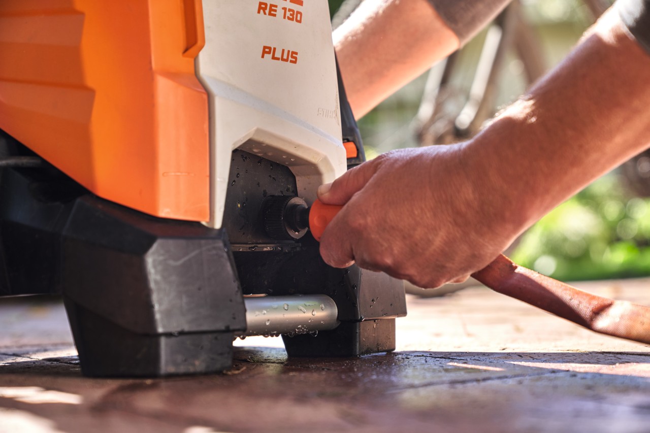 Eine Person schließt einen Gartenschlauch an den Hochdruckreiniger STIHL RE 130 PLUS an, um ihn zu benutzen