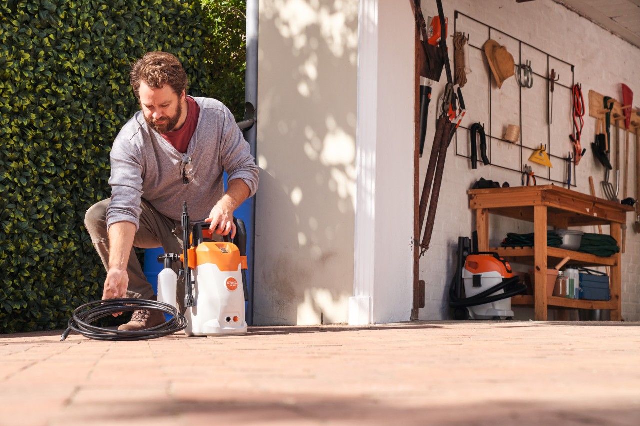 Ein Mann hockt vor einem Werkstatteingang mit einem Hochdruckreiniger STIHL RE 80 X in der Hand