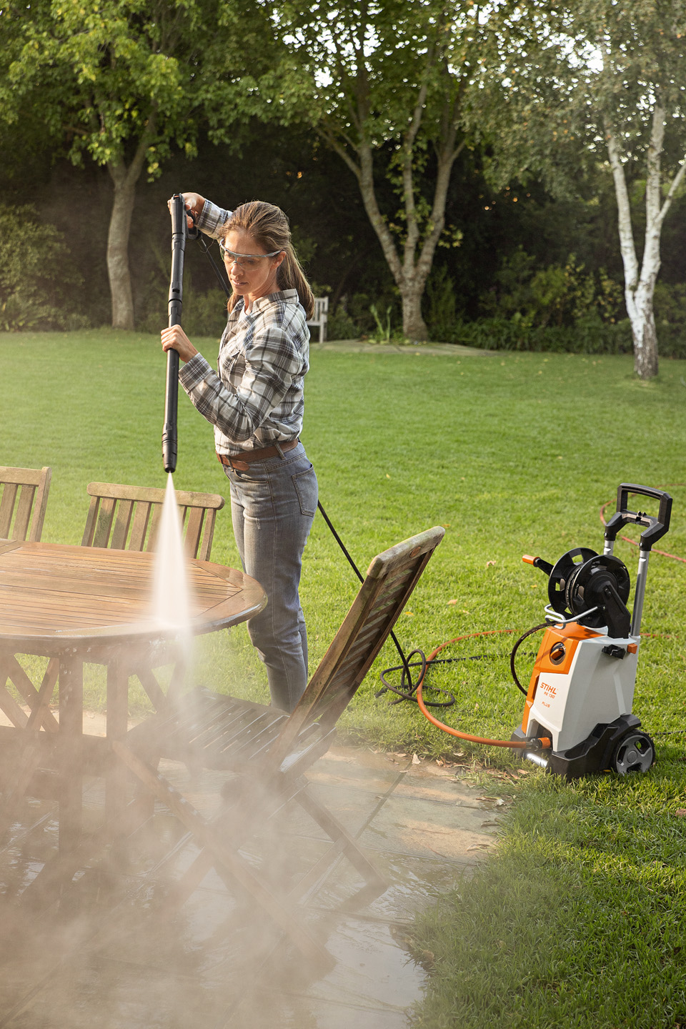 Eine Frau benutzt draußen den Hochdruckreiniger STIHL RE 130 PLUS, um Gartenmöbel zu reinigen