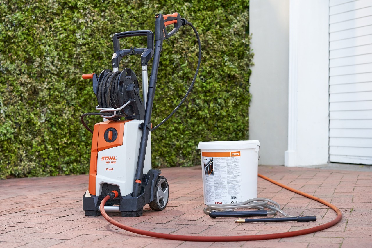 Hochdruckreiniger STIHL RE 130 PLUS und Strahlgranulat SB 90 zum Nassstrahlen vor einer Garage 
