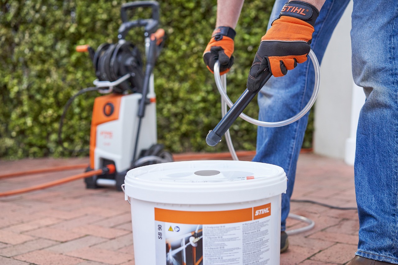 Ein Mann mit Arbeitsschutzhandschuhen vor einer Gartenhecke verwendet das Strahlgranulat STIHL SB 90 zum Nassstrahlen 