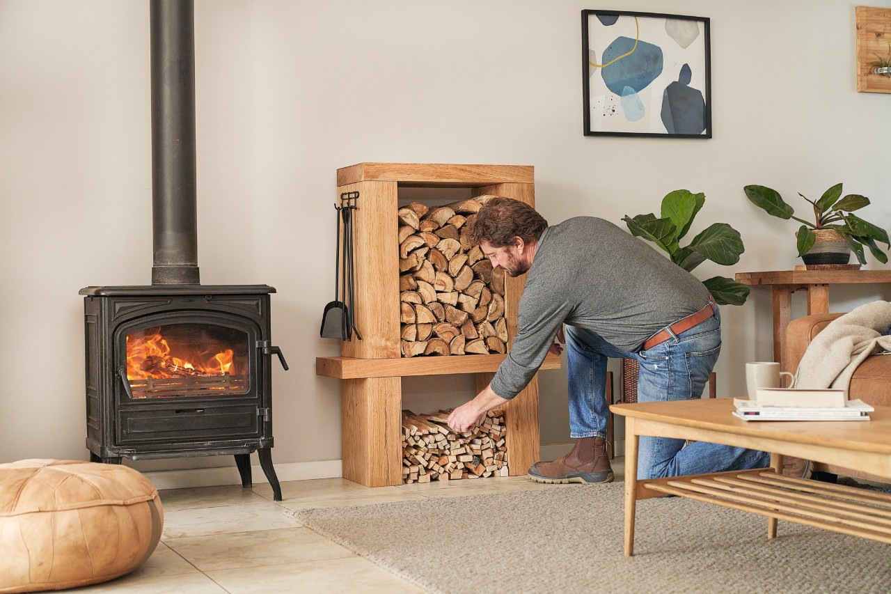 Mann entnimmt einem selbstgebauten Kaminholzregal im Wohnzimmer Holzscheite, um den Kamin zu befüllen