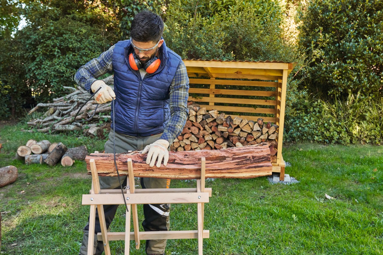 Mann sichert Holz auf dem Sägebock mit einem Spanngummi ab