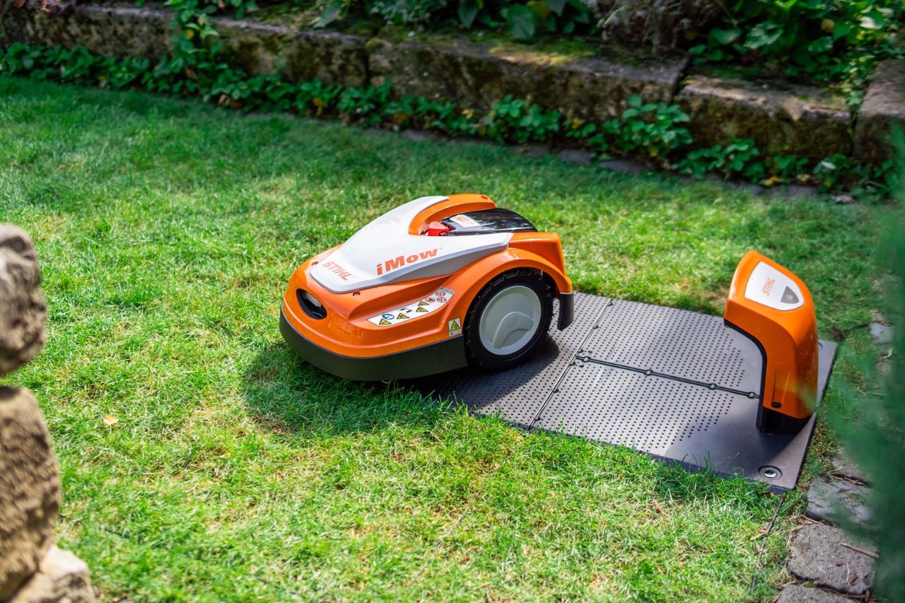STIHL iMOW® Mähroboter neben der Dockingstation auf grünem Rasen 