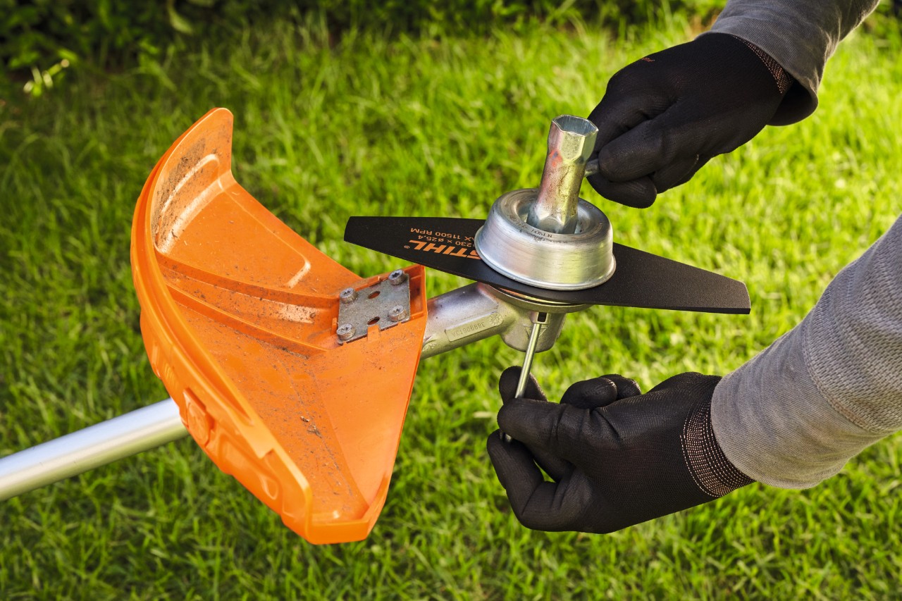 Person mit Schutzhandschuhen prüft Metallwerkzeug einer Motorsense