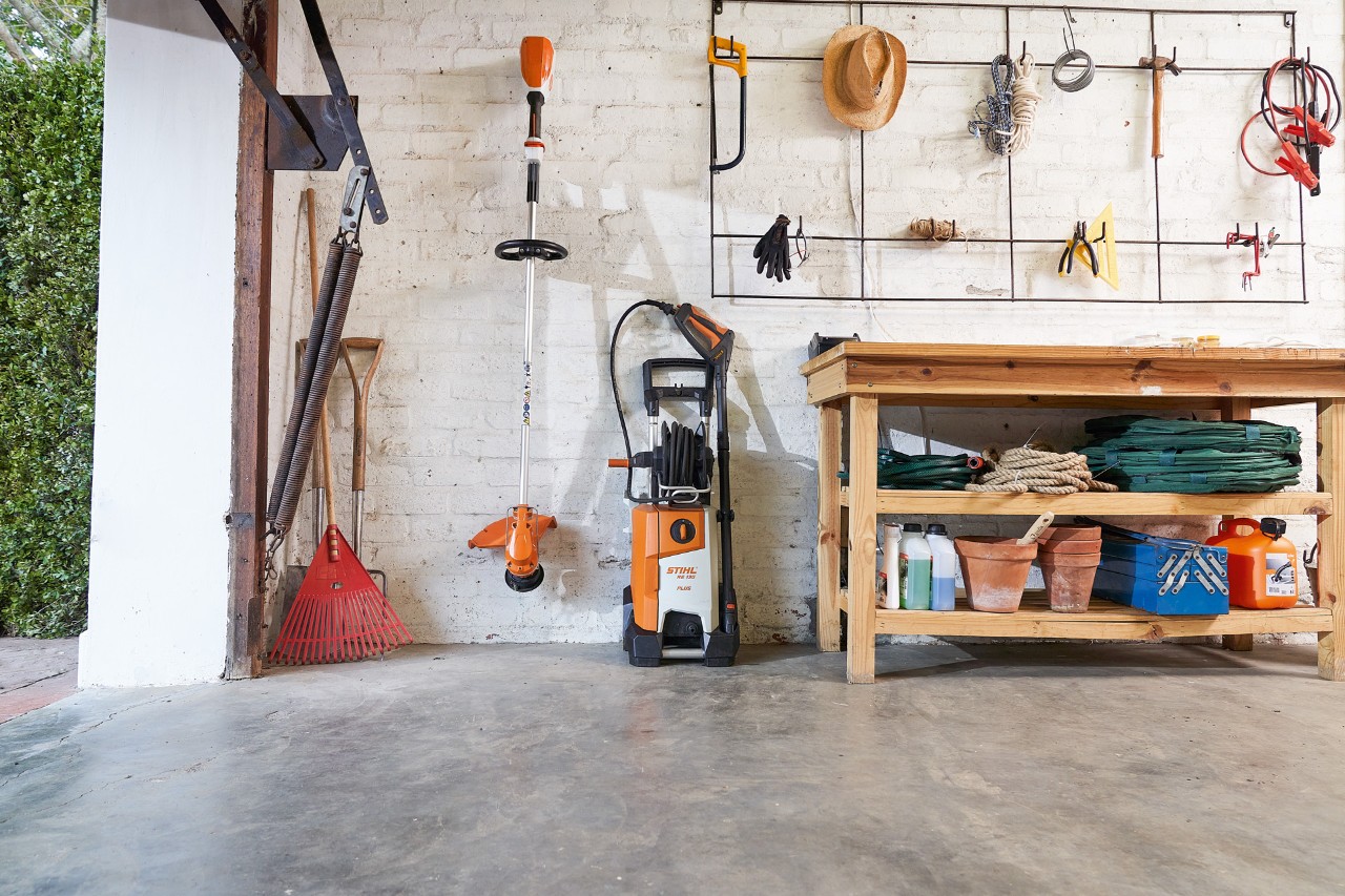 STIHL Akku-Motorsense FSA 56 wird hängend gelagert, daneben Akku-Heckenschere HSA 56 und HLA 56 und Akku-Rasenmäher RMA 339