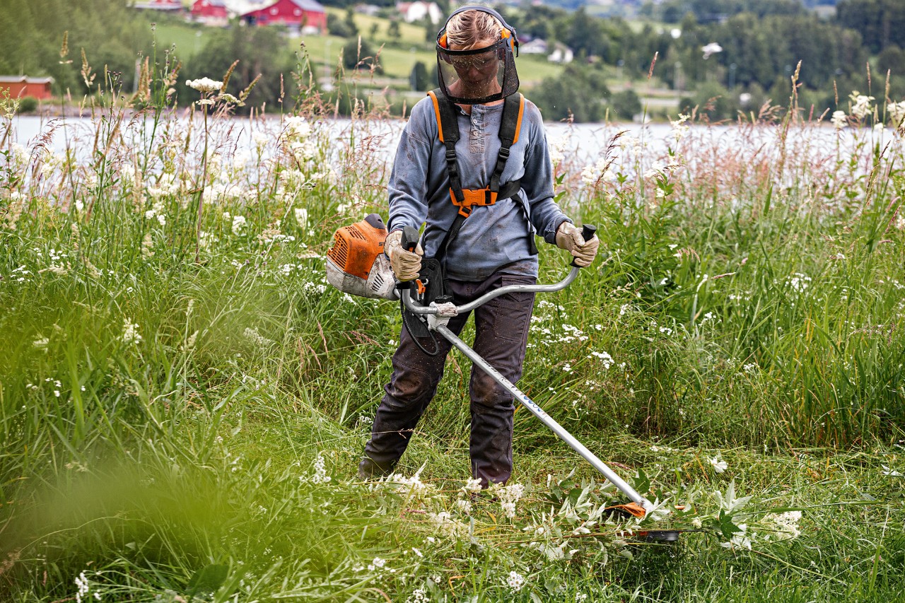 Frau mäht mit STIHL Motorsense FS 240 und Gesichtsschutz hohes Gras an einem See