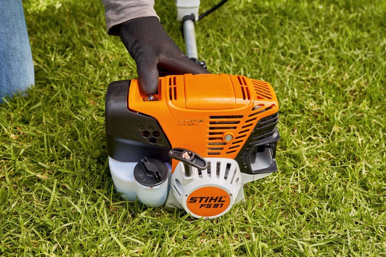 Mann drückt die Kraftstoffpumpe der Benzin-Motorsense STIHL FS 91, um sie zu starten