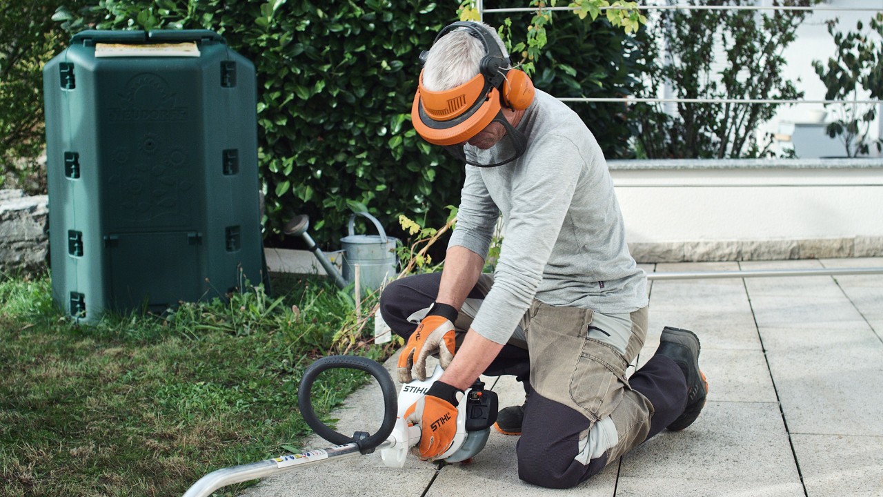 La desbrozadora de gasolina STIHL FS 38 es presionada contra el suelo por una persona con ropa de protección