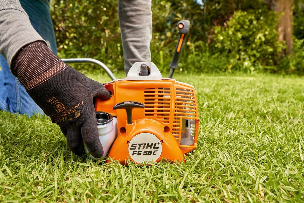 Mann drückt die Kraftstoffpumpe der Benzin-Motorsense STIHL FS 56, um sie zu starten