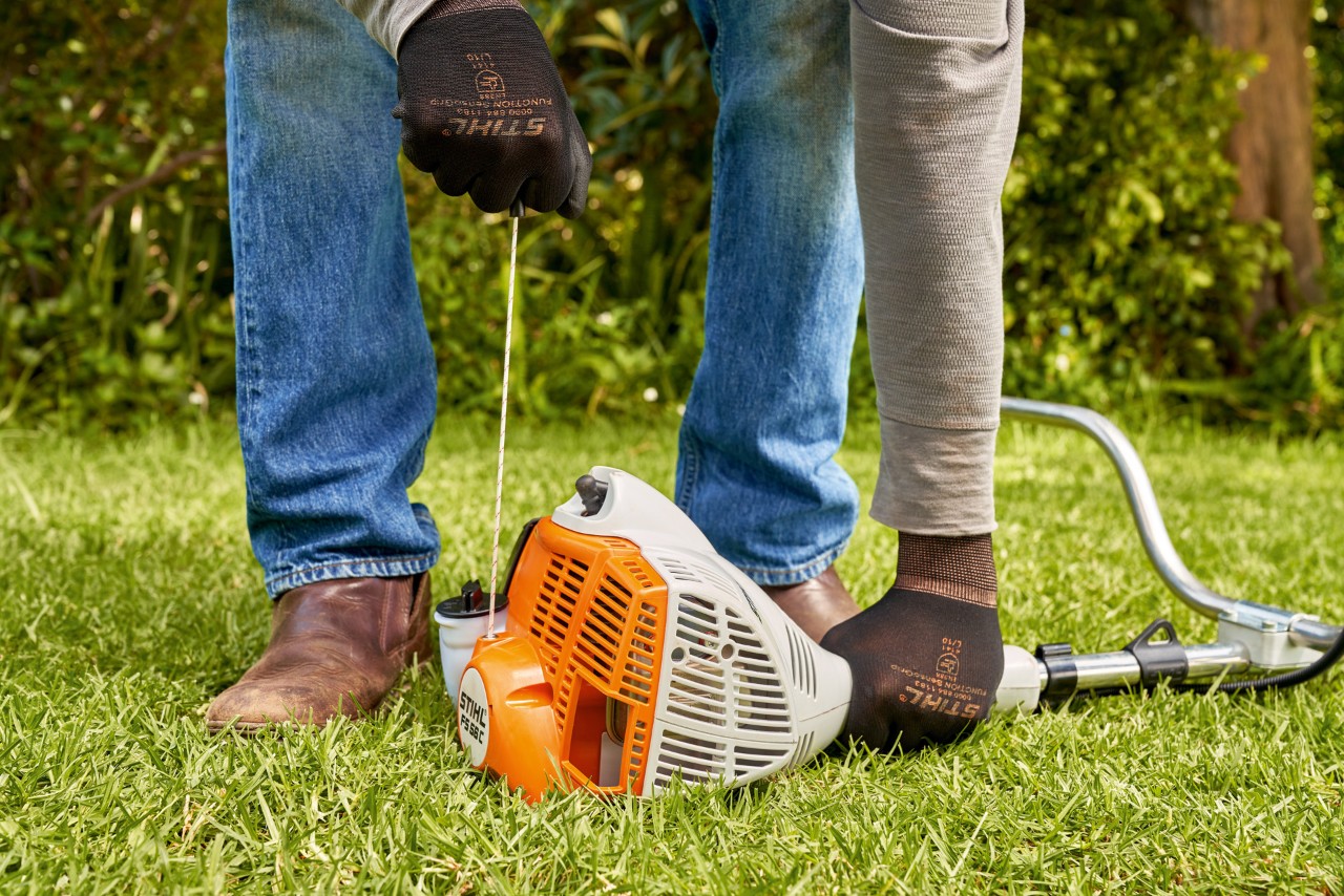 Mann zieht das Anwerfseil der Benzin-Motorsense STIHL FS 56 