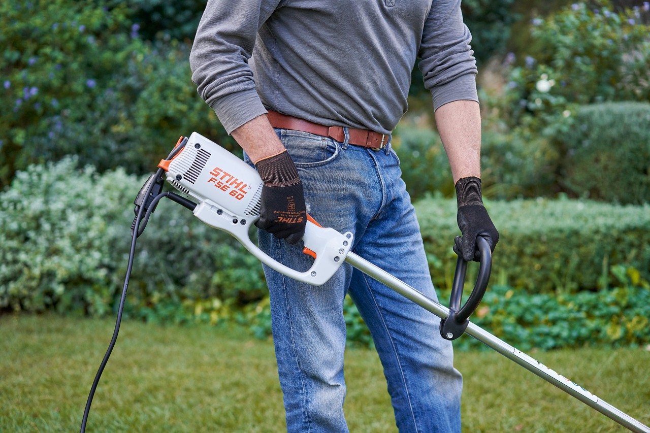 Mann mit Schutzhandschuhen greift die Elektro-Motorsense STIHL FSE 60 mit beiden Händen