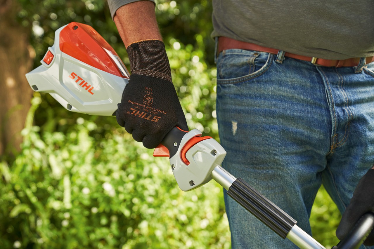 Mann mit Schutzhandschuhen drückt die Schalthebelsperre der Akku-Motorsense STIHL FSA 60 