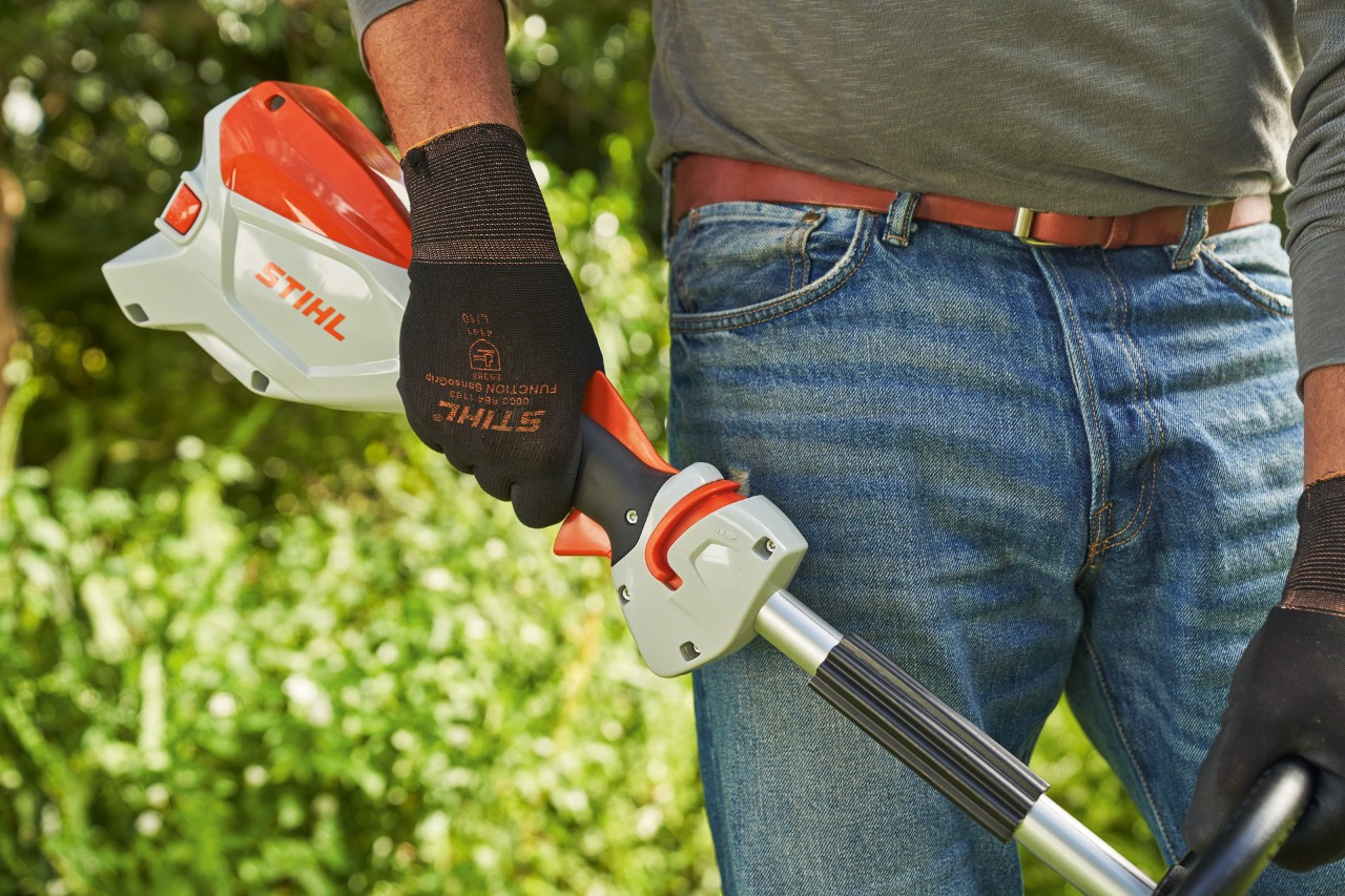 Mann mit Schutzhandschuhen lässt den Schalthebel der Akku-Motorsense STIHL FSA 60 los, um sie auszuschalten