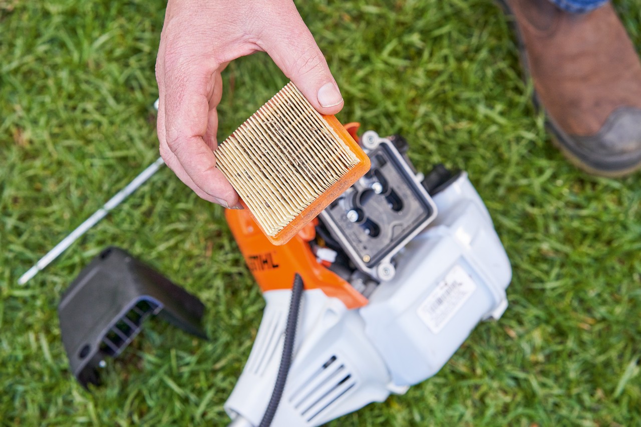 Eine Person entnimmt den Luftfilter einer STIHL Motorsense, um ihn zu reinigen 