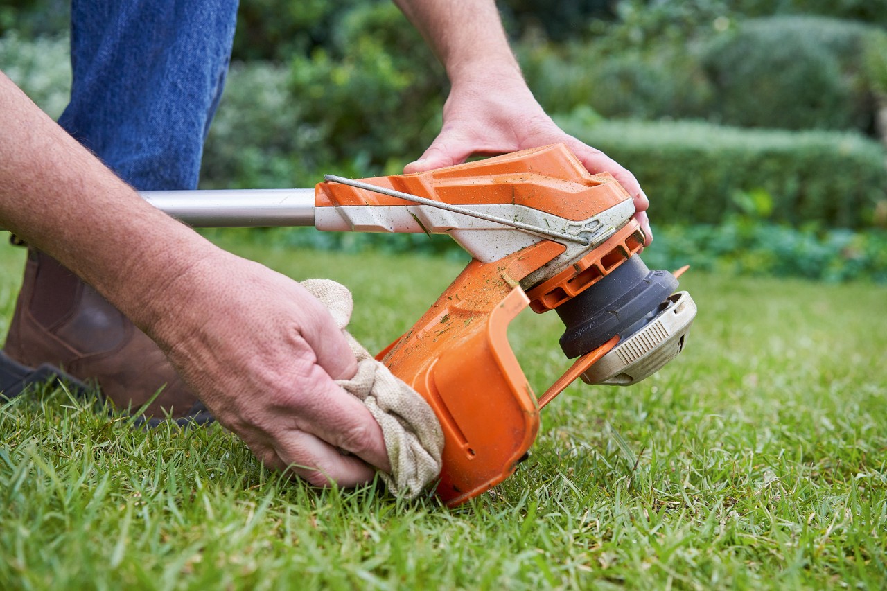 Eine Person reinigt mit einem feuchten Tuch den Schutz einer STIHL Motorsense