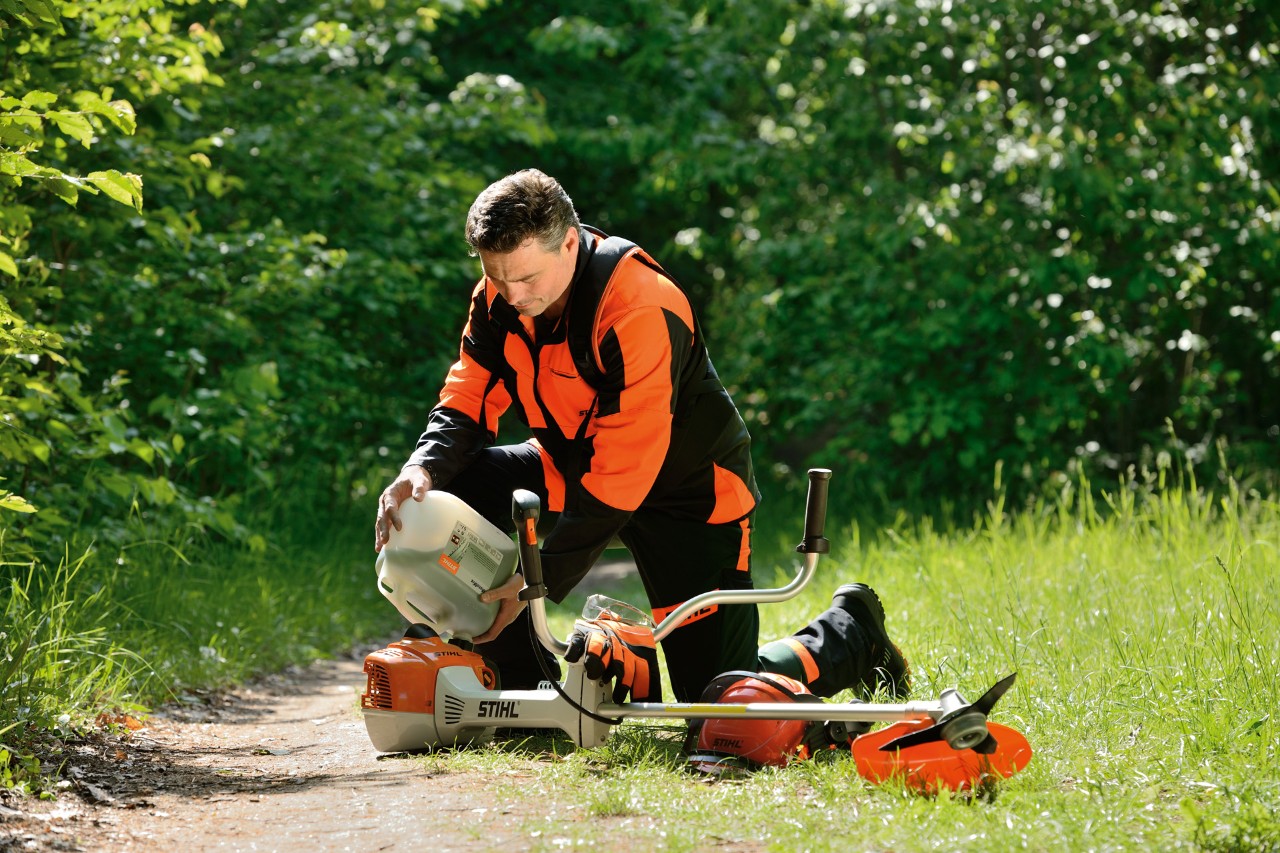 Mann in STIHL Schutzausrüstung betankt eine STIHL Motorsense mit einem Benzin-Öl-Gemisch