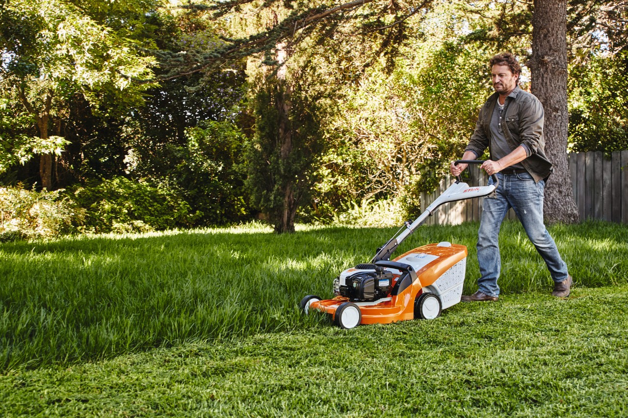 Ein Mann mäht in einem Garten den Rasen mit einem STIHL Rasenmäher 