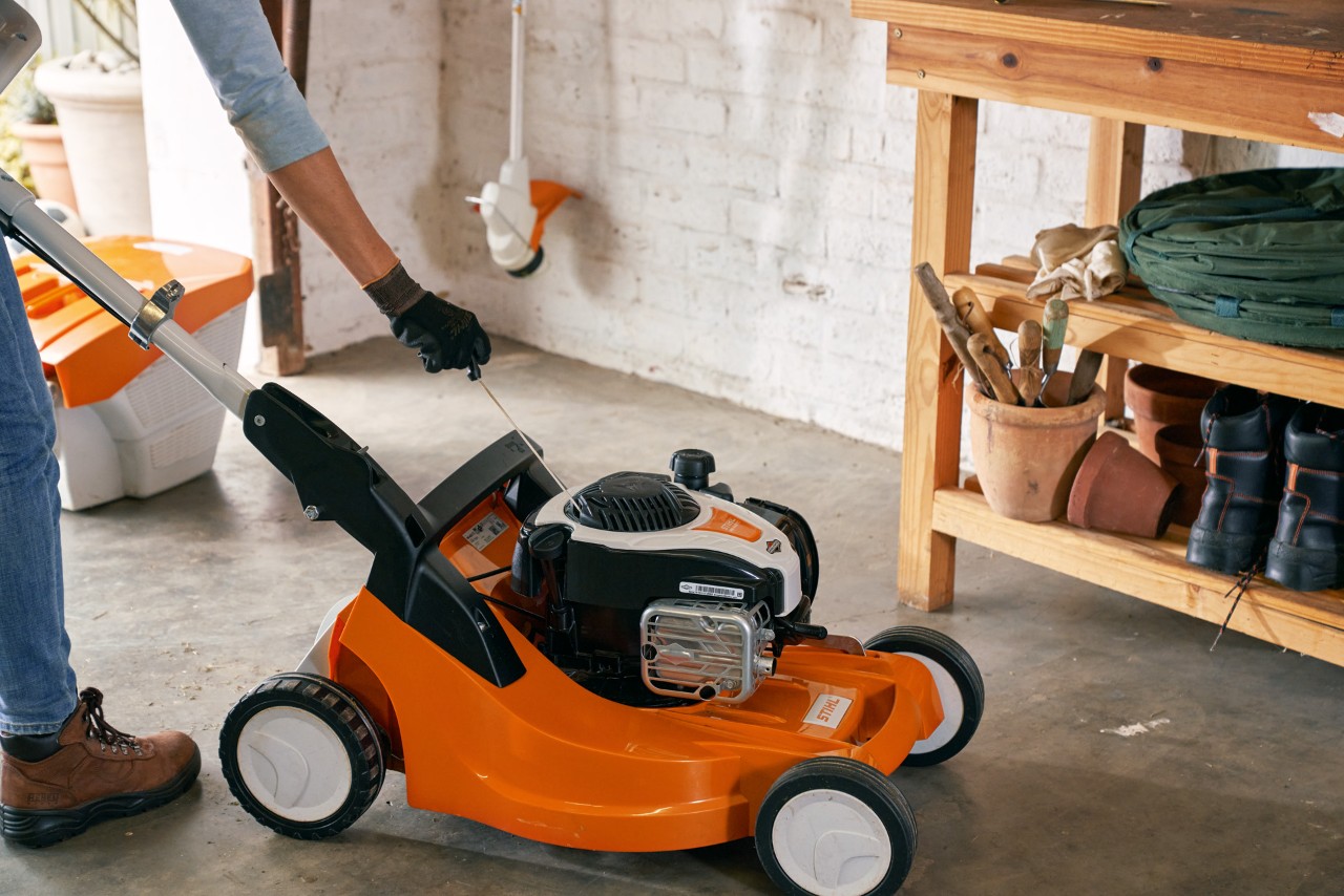 Person reinigt in einer Garage den Luftfilter eines STIHL Benzin-Rasenmähers RM 448 TC