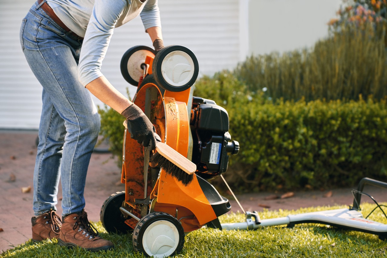 Frau reinigt STIHL Benzin-Rasenmäher RM 448 T-C mit einem Handfeger