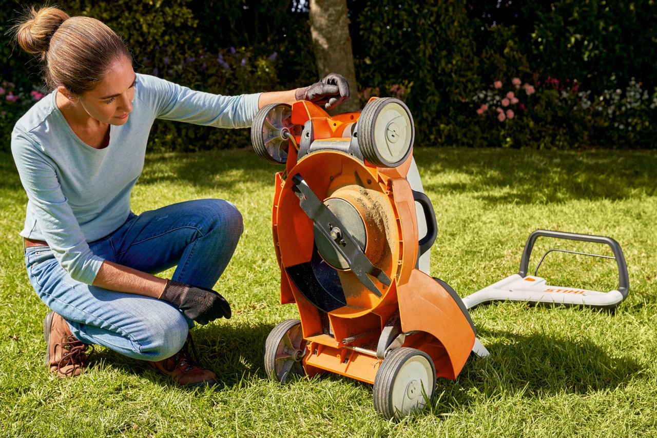 Frau schaut im Garten unter ihren STIHL Akku-Rasenmäher RMA 339C