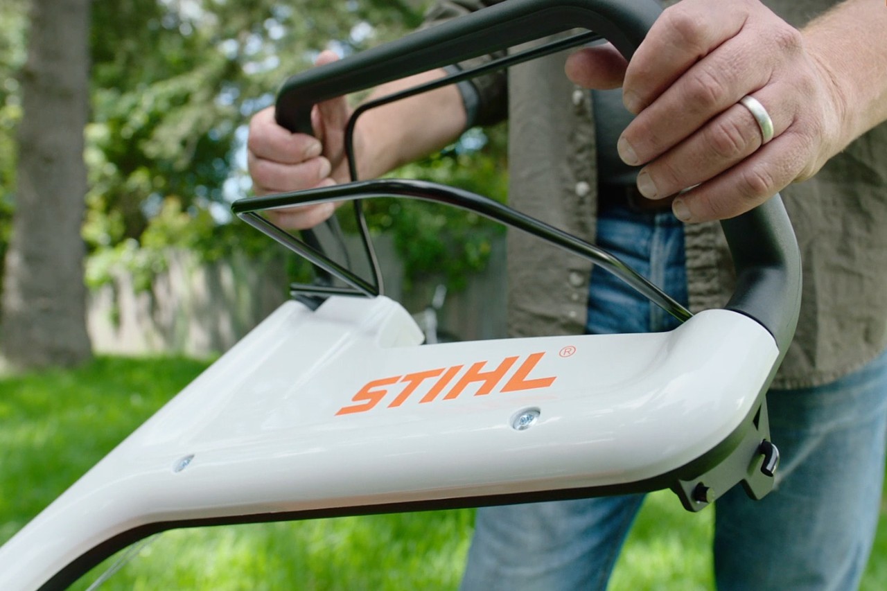 Eine Person drückt den Motorstoppbügel eines STIHL Rasenmähers