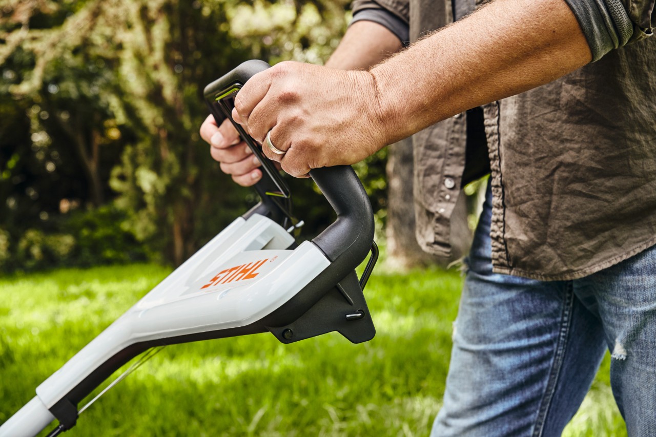 Ein Mann hält den Benzin-Rasenmäher STIHL RM 448 TC am Lenker fest, um den Rasen zu mähen