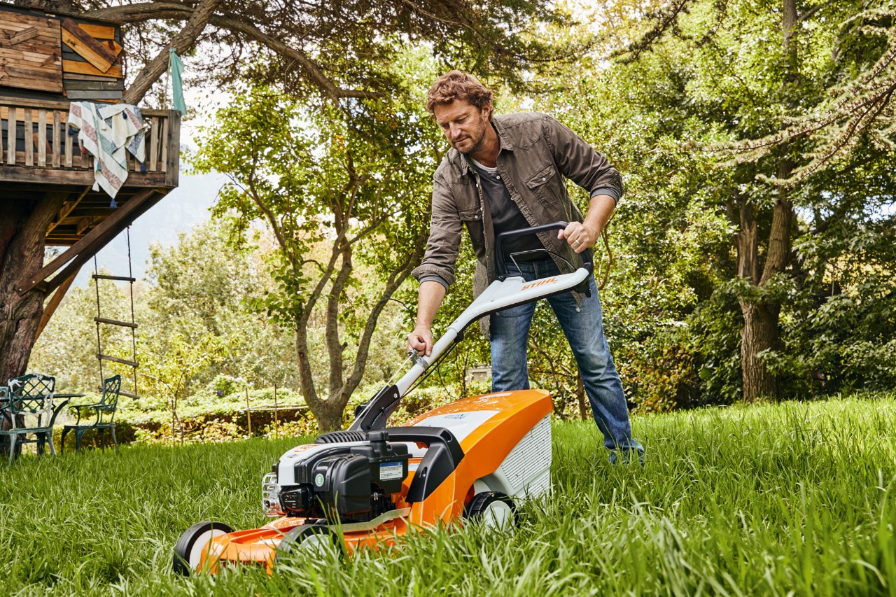 Ein Mann auf einem Gartengrundstück mäht den Rasen mit einem STIHL Rasenmäher mit STIHL 4-Takt-Motor