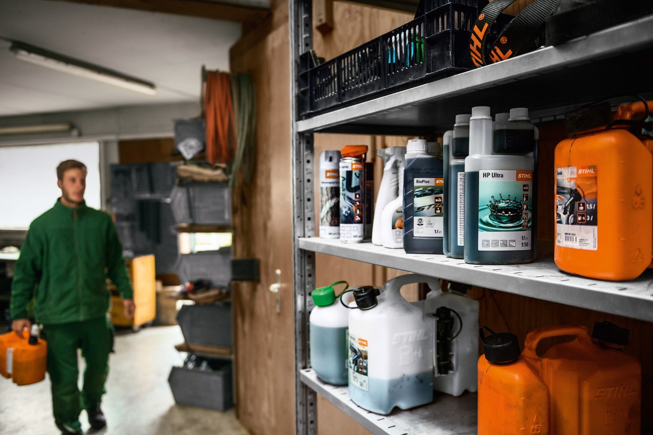 Ein Mann in einer Garage mit STIHL Betriebsstoffen, um den Rasenmäher zu tanken