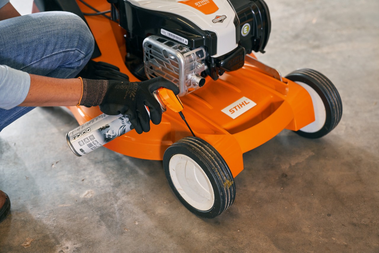 Bewegliche Teile am STIHL Benzin-Rasenmäher RM 448 TC werden eingefettet, um ihn winterfest zu machen