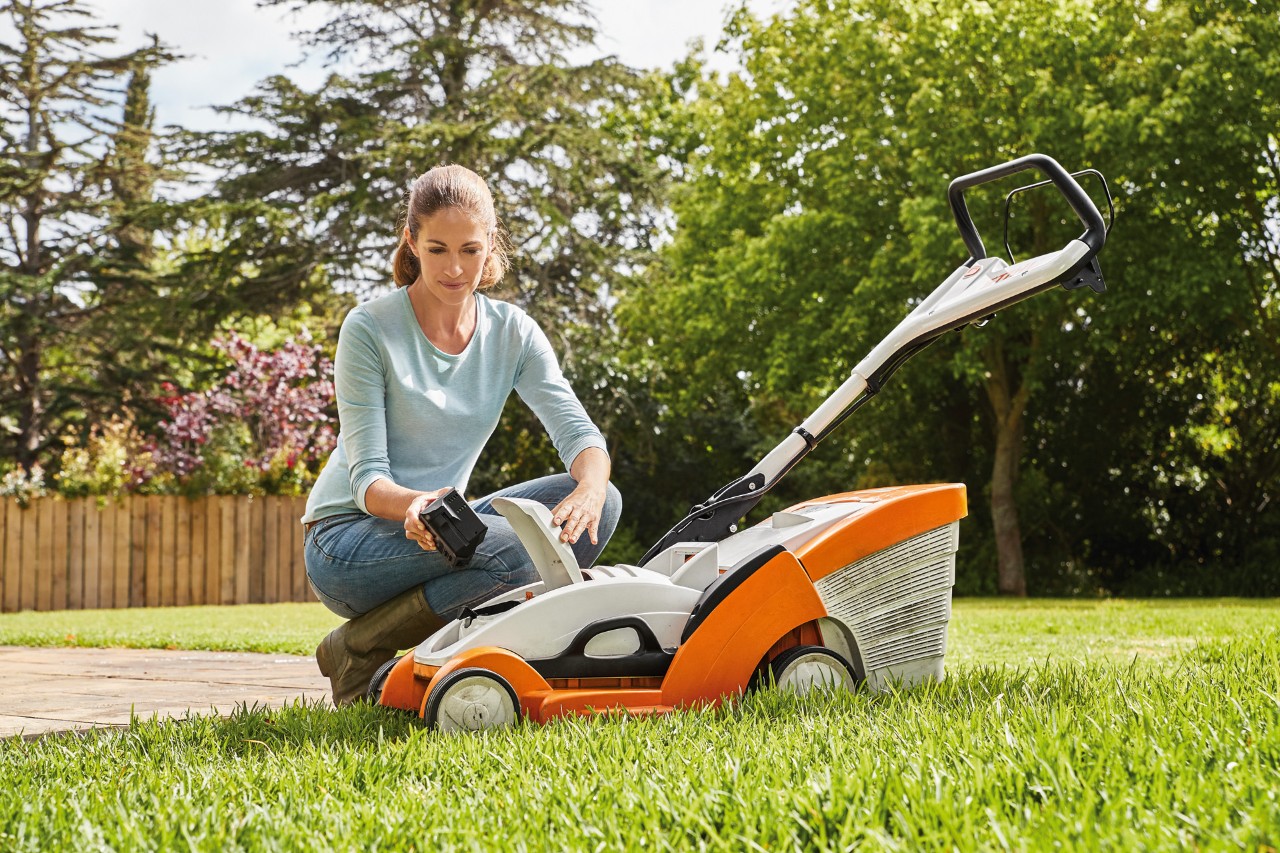 Eine Frau kniet neben einem STIHL Akku-Rasenmäher RMA 339 C und entfernt den Akku