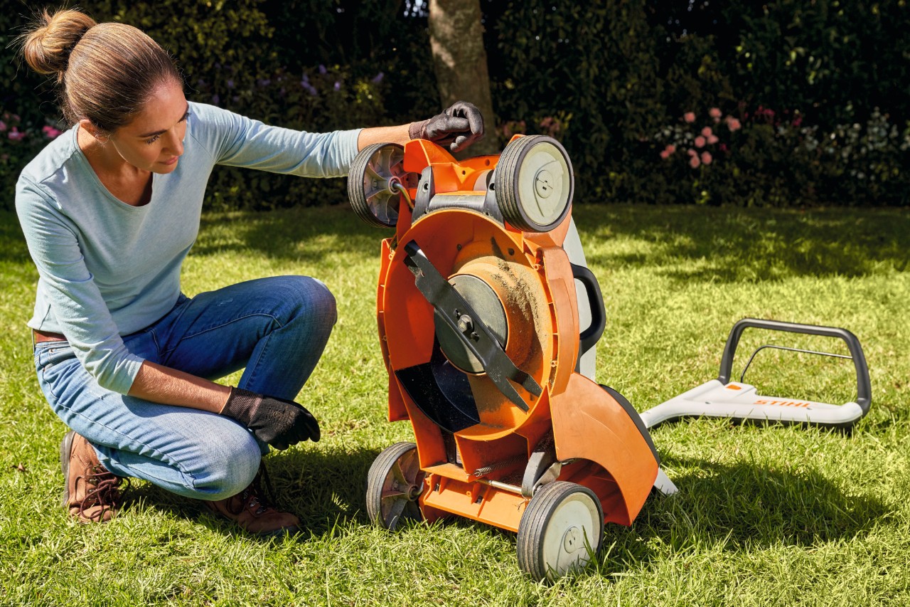 Eine kniende Frau betrachtet das Mähwerk des STIHL Rasenmähers RMA 399 C.