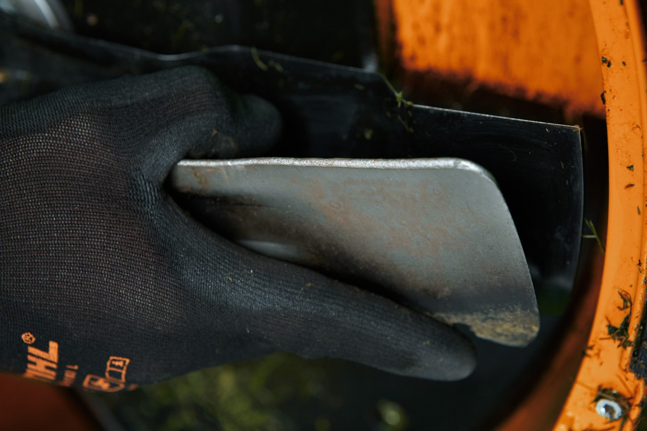 Rasenmähermesser an Unterseite von STIHL Rasenmäher wird mit Spatel gereinigt, um sie anschließend zu schärfen.