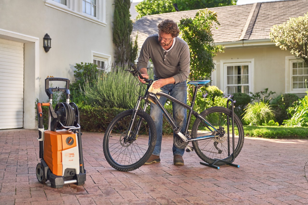 Mann trocknet Fahrrad nach dem Waschen mit einem Tuch ab, daneben steht ein STIHL Hochdruckreiniger RE 130 plus