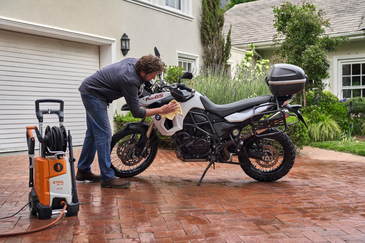Mann trocknet Motorrad nach der Reinigung, daneben steht ein STIHL Hochdruckreiniger RE 130 plus