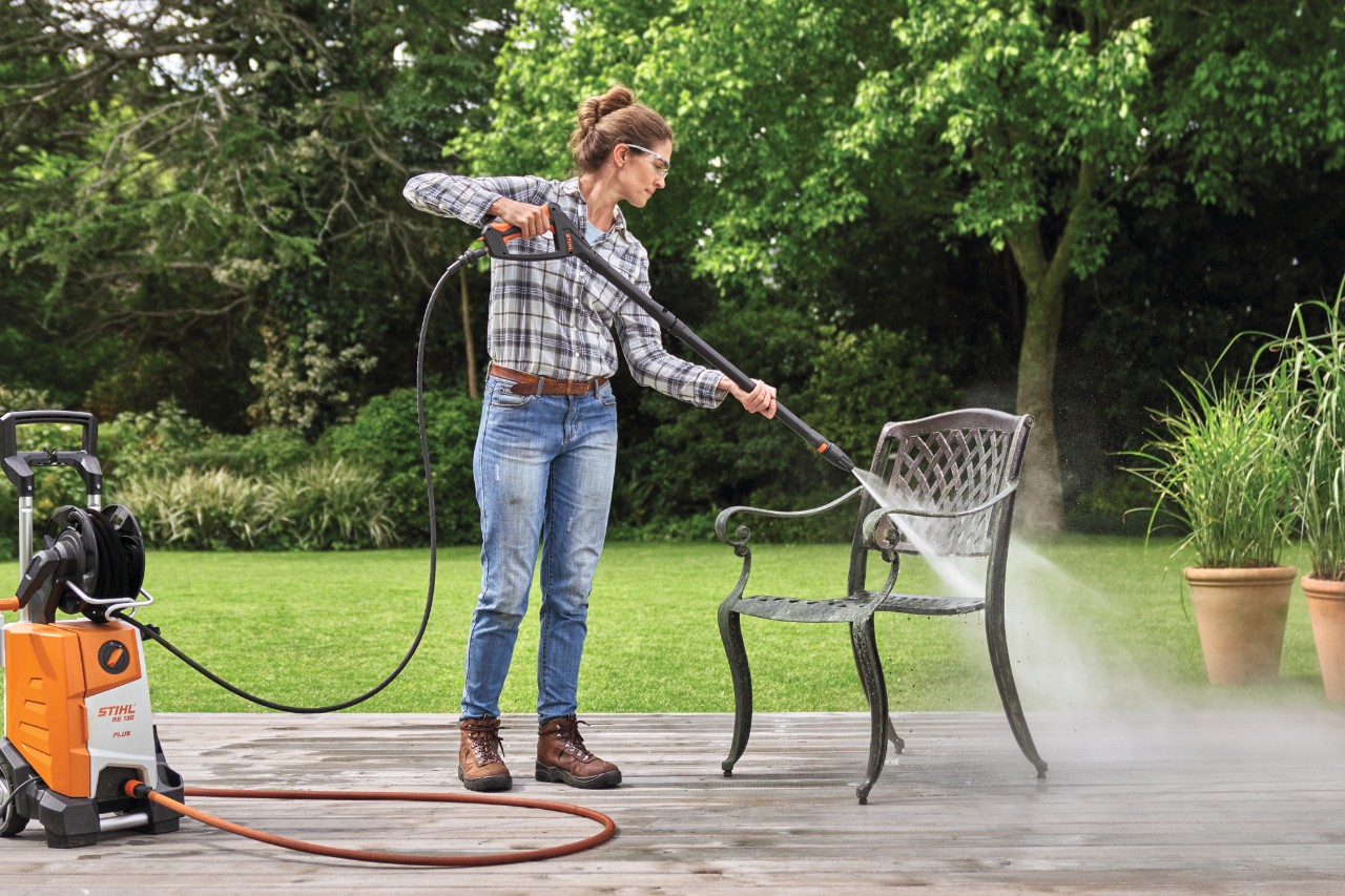 Frau reinigt Gartenstuhl aus Metall auf der Terrasse mit dem STIHL Hochdruckreiniger RE 130 plus 