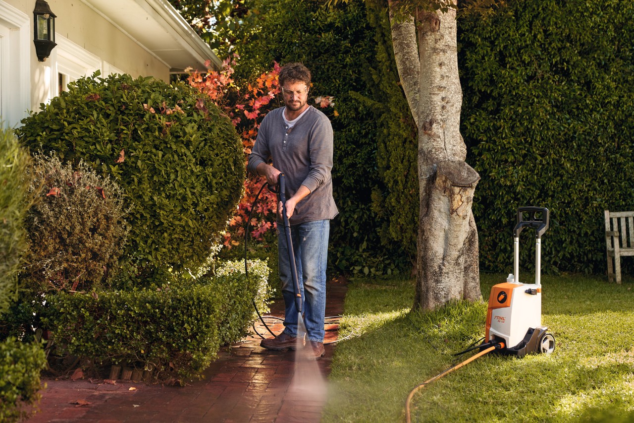 Mann reinigt Pflastersteine vor seinem Haus mit STIHL Hochdruckreiniger RE 110