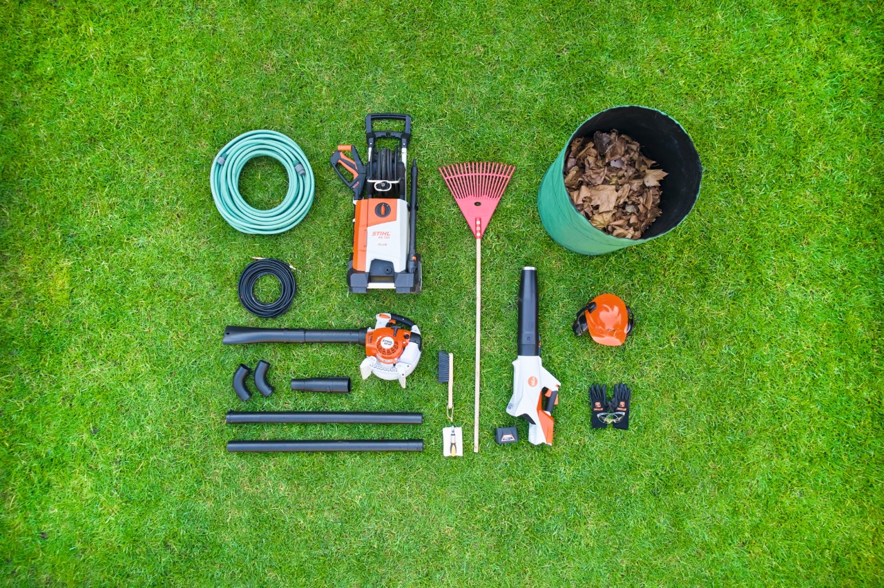 Einzelteile des STIHL Dachrinnenreinigungssets liegen ordentlich nebeneinander sortiert auf einer Rasenfläche 